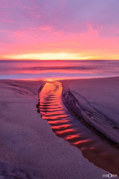 Crimson sunrise reflections flowing through a water channel into Lake Macquarie at dawn