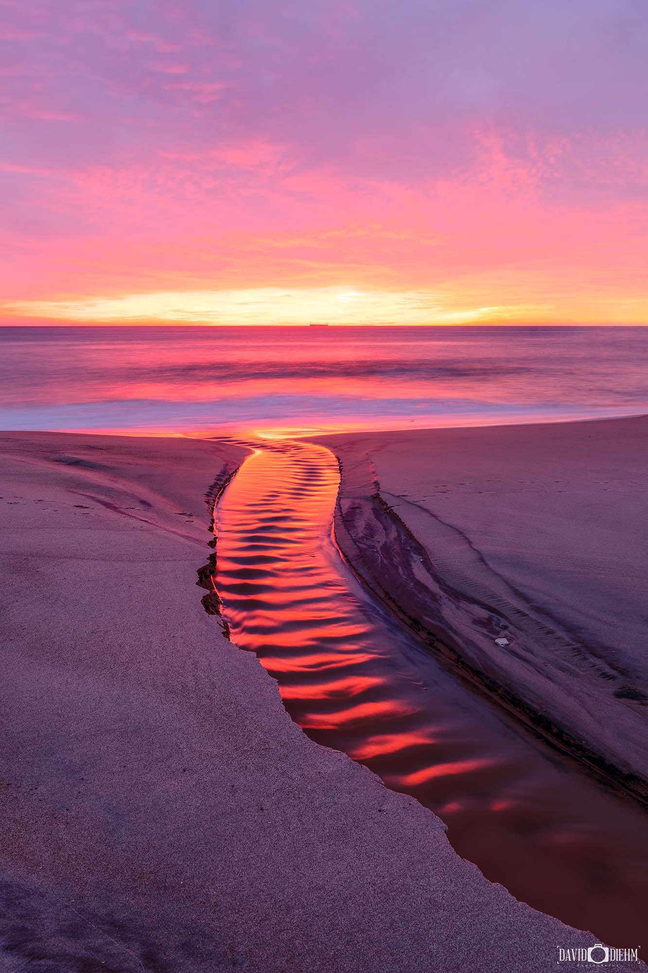 Crimson sunrise reflections flowing through a water channel into Lake Macquarie at dawn