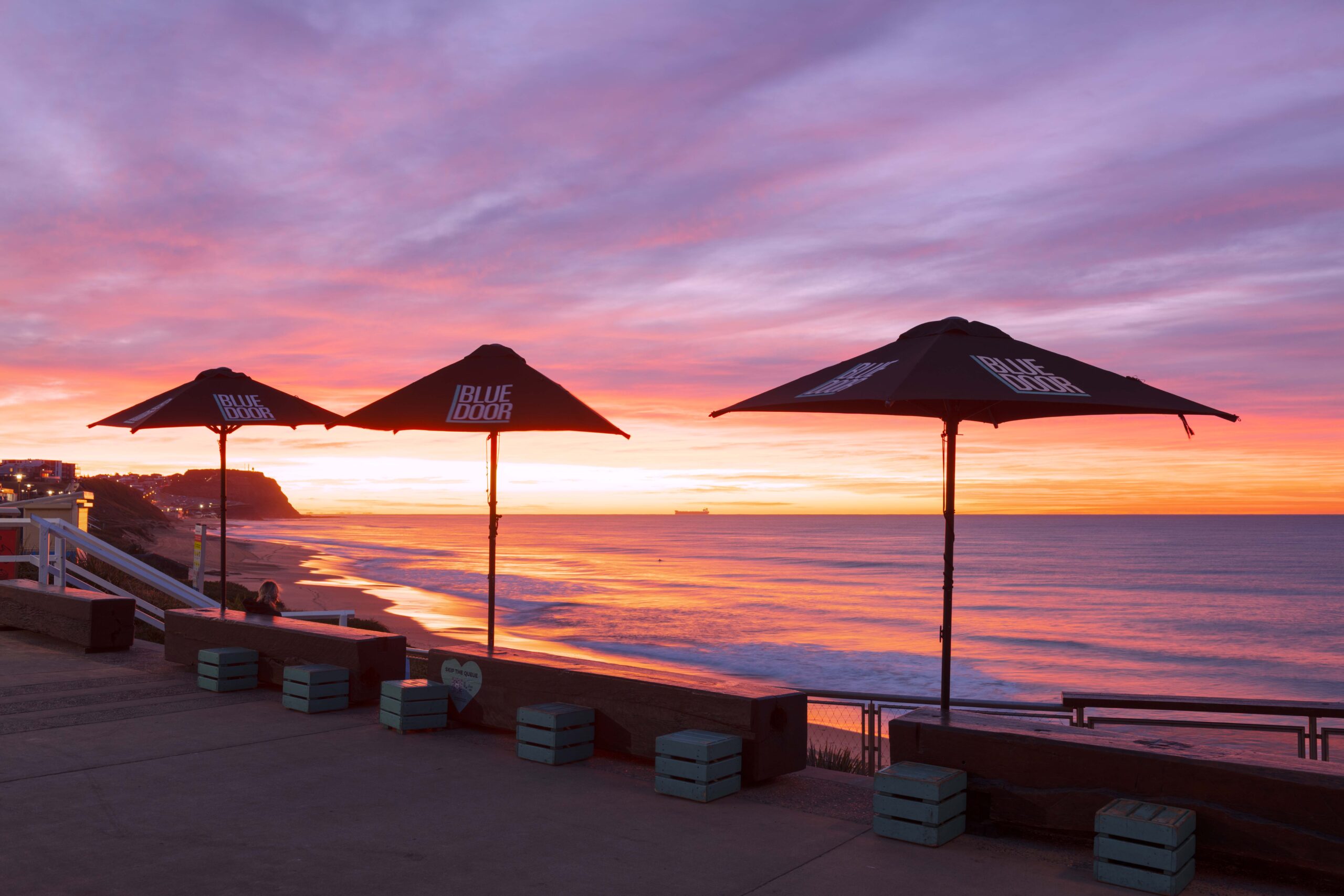 Sunrise at Merewether Beach with classic umbrella beside the blue door kiosk in Newcastle NSW