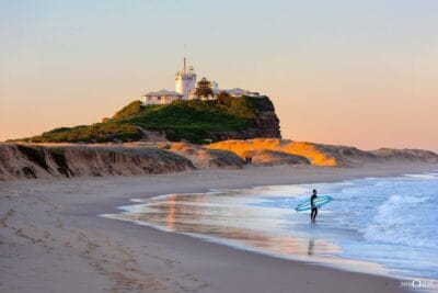 Nobby's Beach at sunset on a clear afternoon with a lone surfer riding the waves, capturing the golden light and tranquil coastline of Newcastle, NSW