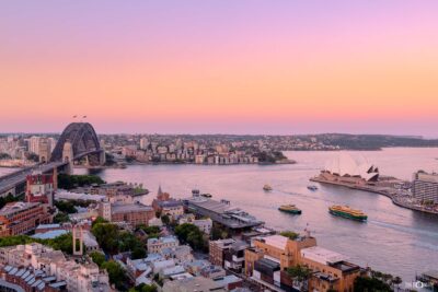 Photograph of Sydney Harbour at sunset with warm golden light reflecting on the water and skyline.