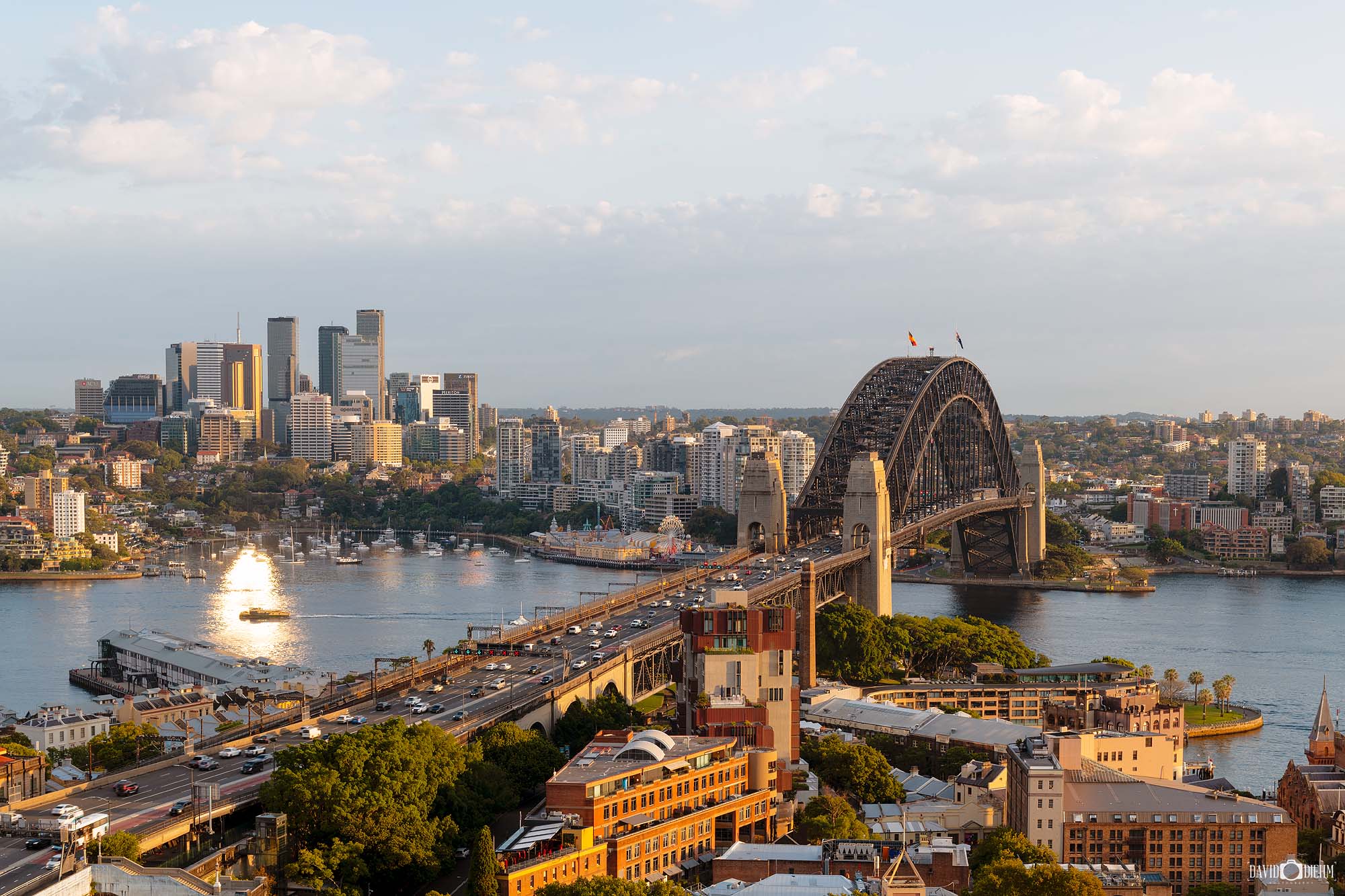 Photograph of the Sydney Harbour Bridge illuminated by soft morning sunrise light over Sydney Harbour with warm sky tones and reflections
