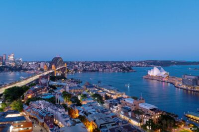 Photograph of Sydney Harbour at twilight with glowing city lights, waterfront reflections, and skyline views during the evening.