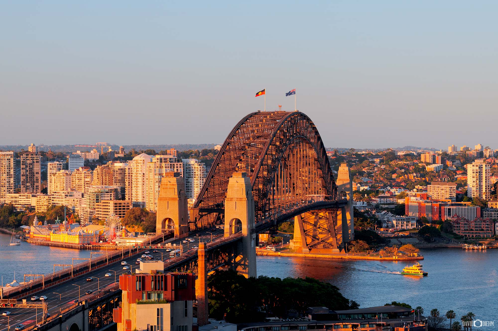 Photograph of the Sydney Harbour Bridge at sunset with warm sky tones and reflections over Sydney Harbour.