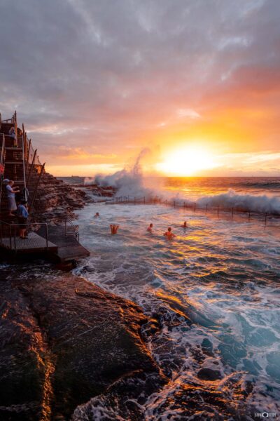 Swimmers at Bogey Hole in Newcastle captured at sunrise with waves breaking into the ocean rock pool