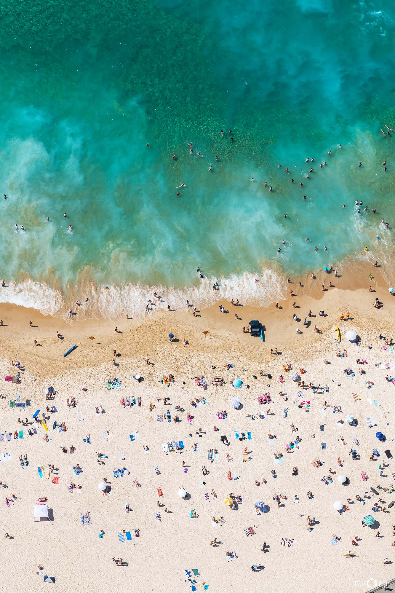 Aerial photograph of people enjoying Bondi Beach in Sydney, showing beach activity, swimmers, and surfers from above.