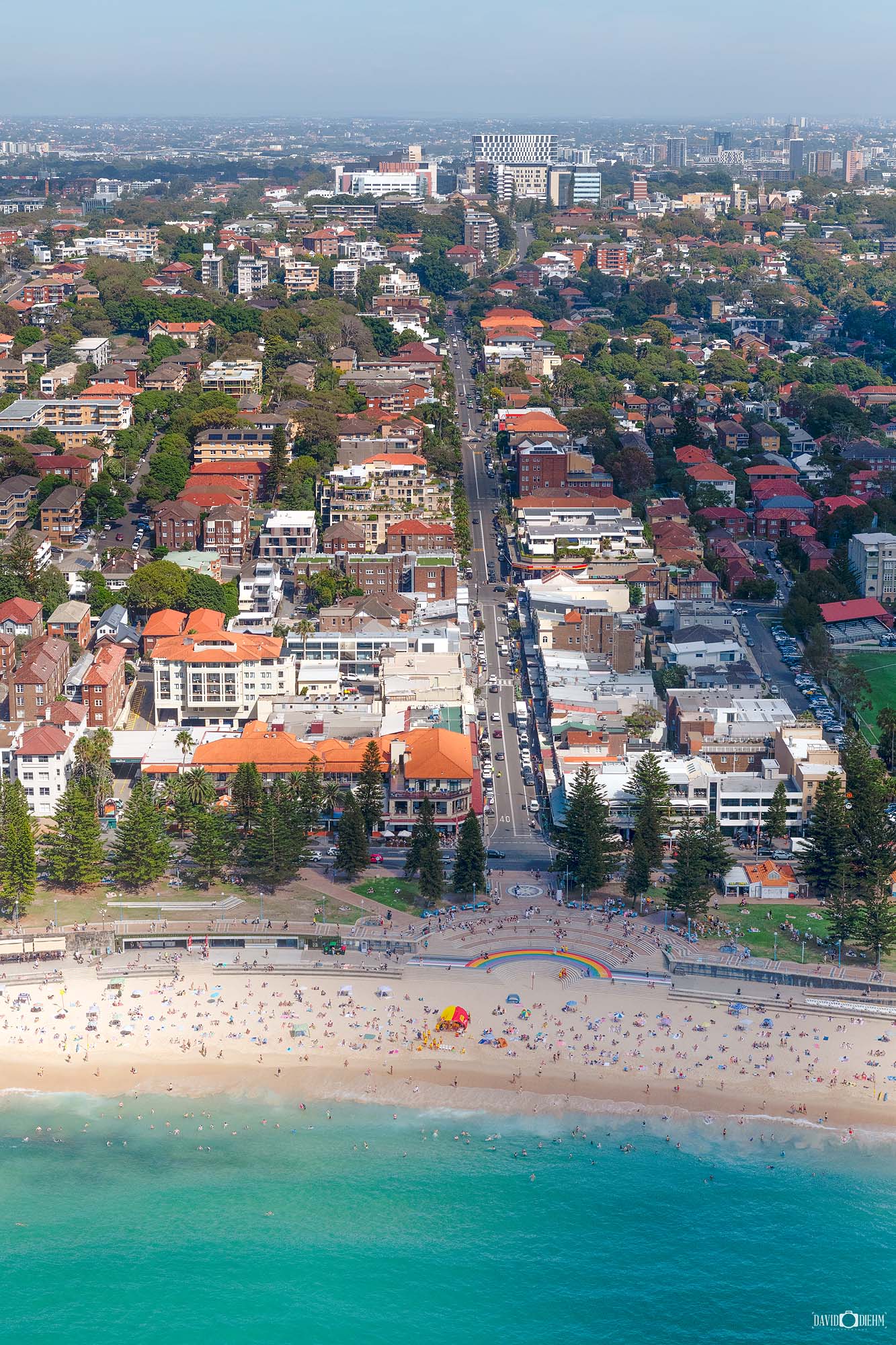Aerial photograph of Coogee Beach in Sydney, showing the curved shoreline, ocean pools, and coastal reserve from above.