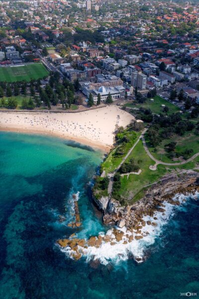 Aerial photograph of Coogee Beach in Sydney capturing the sweeping bay, rocky headland, and surrounding coastal cliffs from above.