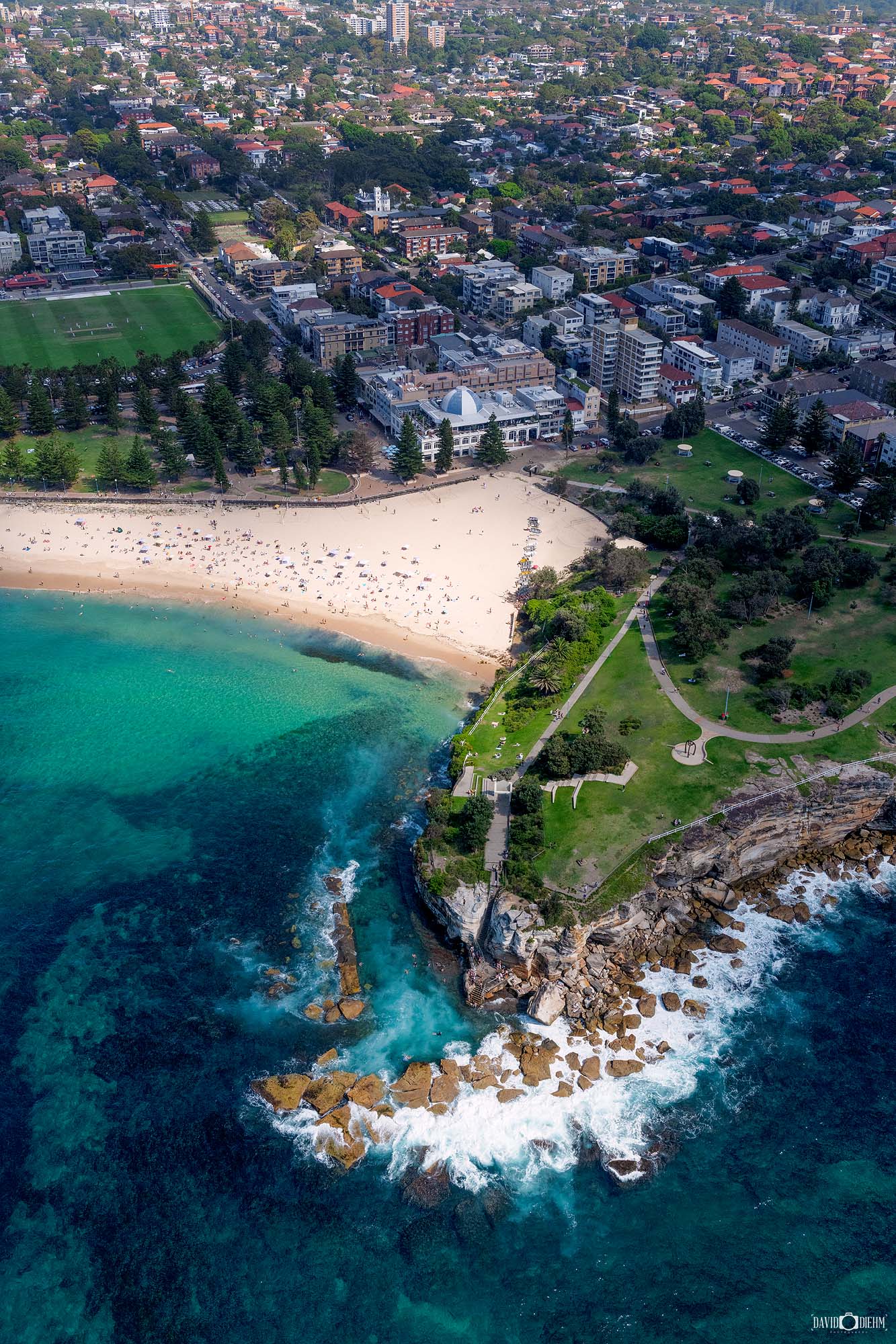 Aerial photograph of Coogee Beach in Sydney capturing the sweeping bay, rocky headland, and surrounding coastal cliffs from above.