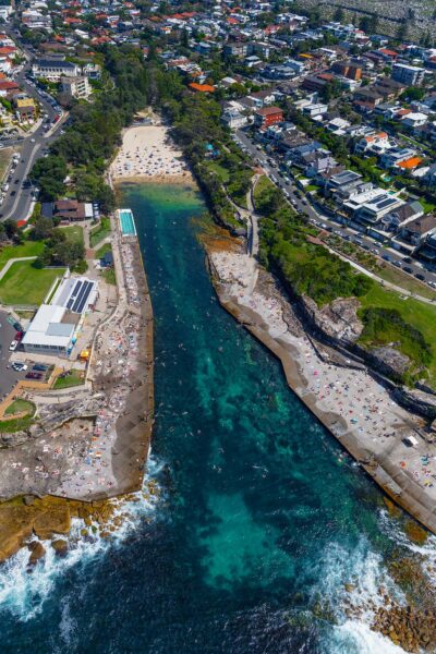 Aerial photograph of Clovelly Beach in Sydney, Australia, showing the narrow bay, clear water, and rocky coastline from above.
