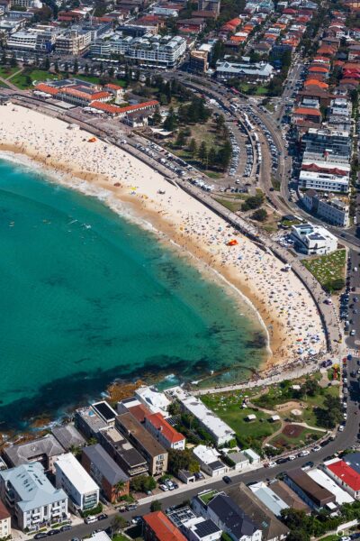 Aerial photograph of Bondi Beach in Sydney, Australia, showing the sweeping shoreline, surf, and vibrant coastline from above.