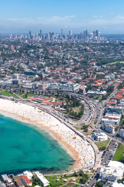 Aerial view of Bondi Beach on a picture-perfect summer day with crowds, turquoise water and Sydney city in the background