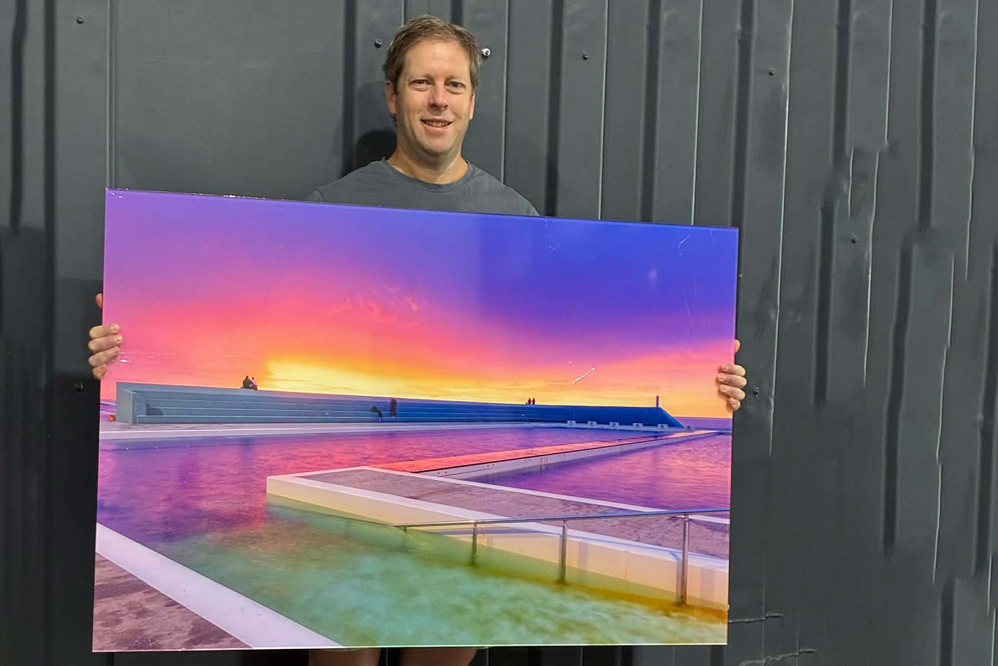 David Diehm holding a Newcastle Ocean Baths acrylic print in a modern studio setting