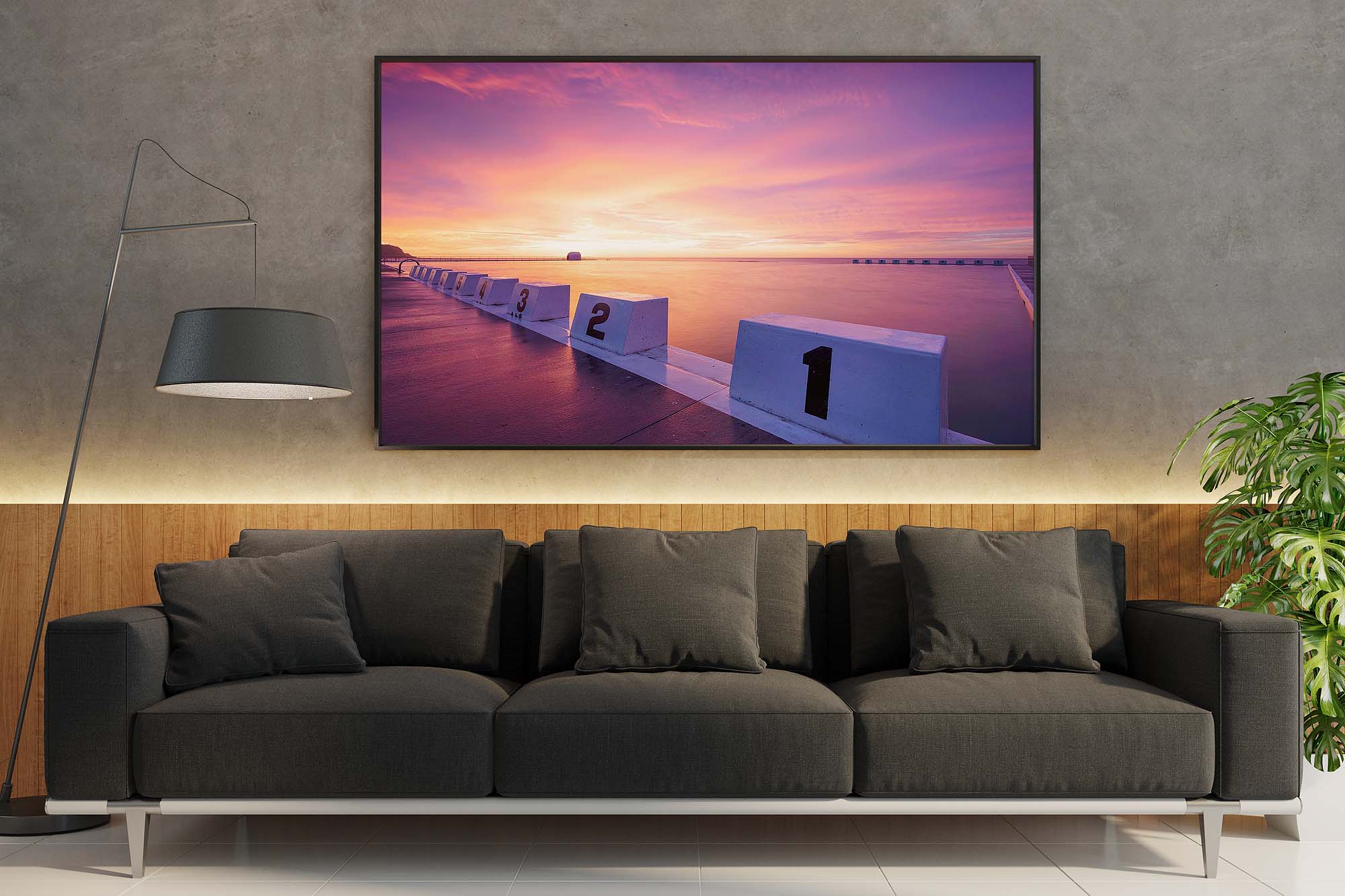 Wall mockup featuring a framed Merewether Ocean Baths sunrise photograph, showcasing warm morning light, ocean waves, and a coastal interior setting.