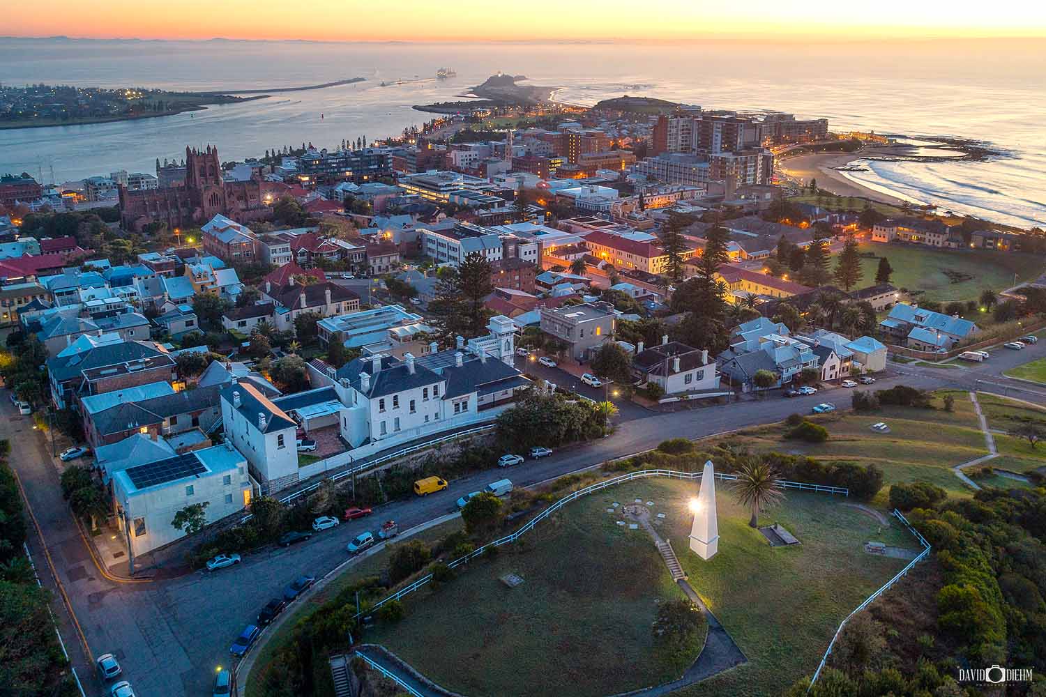 An aerial view of The Obelisk overlooking Newcastle Harbour, Nobbys Headland and the Newcastle skyline at twilight.