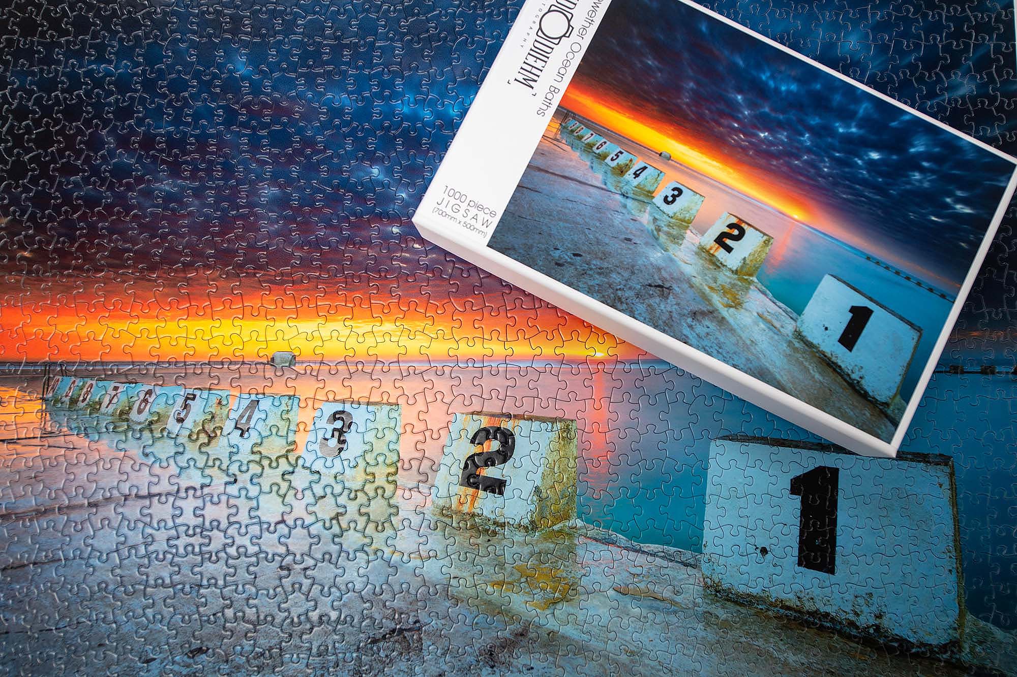 Merewether Ocean Baths jigsaw puzzle showing the puzzle box and pieces featuring the iconic ocean baths in Newcastle with coastal waves and seaside scenery.