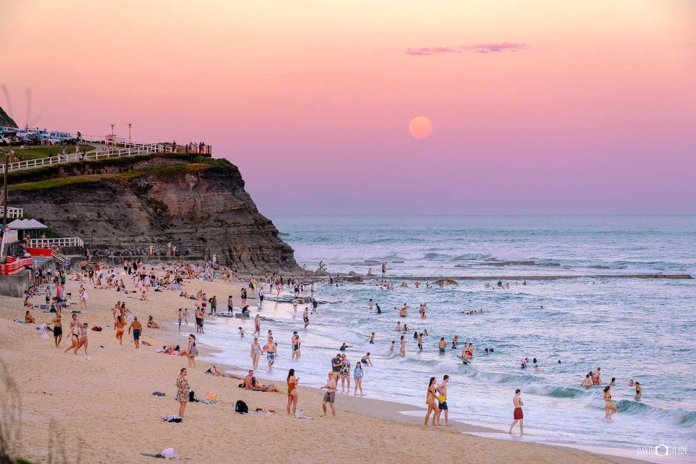 Bar Beach Newcastle at dusk with beachgoers enjoying the coastline beneath pastel evening skies