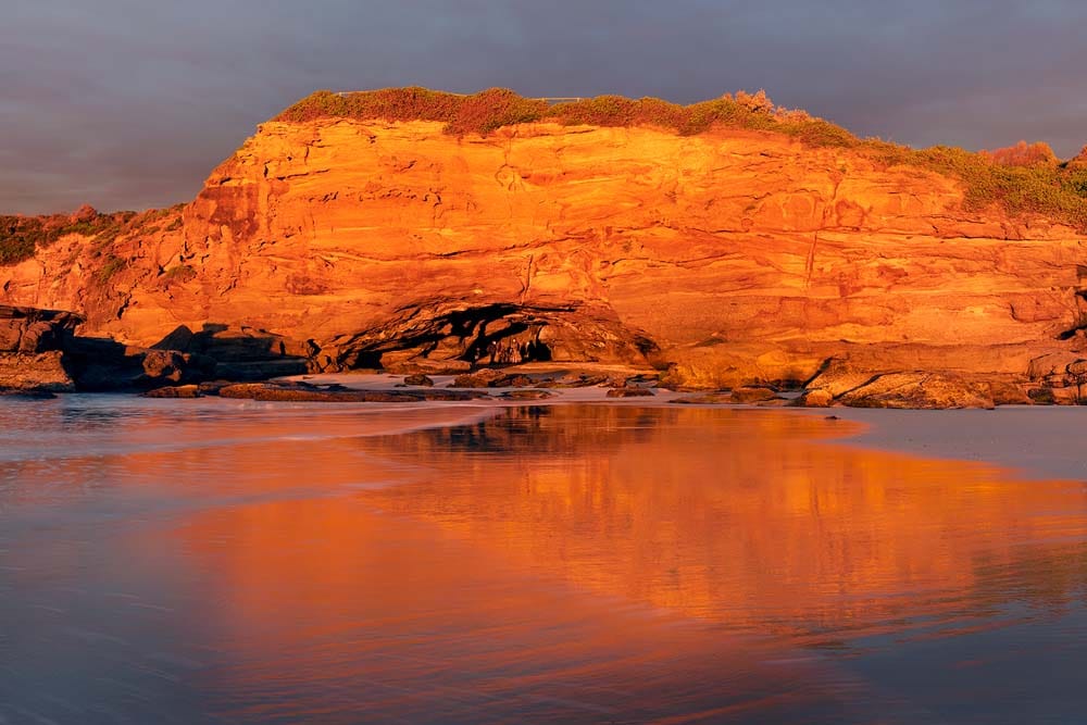 Golden sunrise viewed from inside the sea caves at Caves Beach with sandstone formations and ocean reflections
