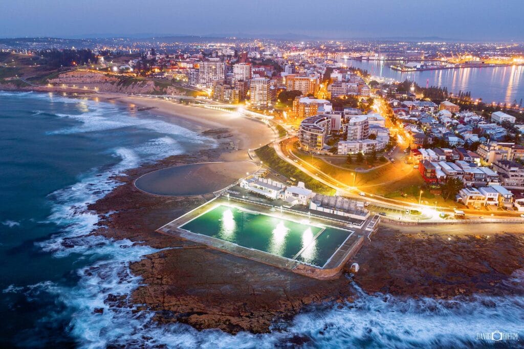 Aerial view of Newcastle Ocean Baths and Newcastle city skyline illuminated at dusk, Newcastle NSW Australia