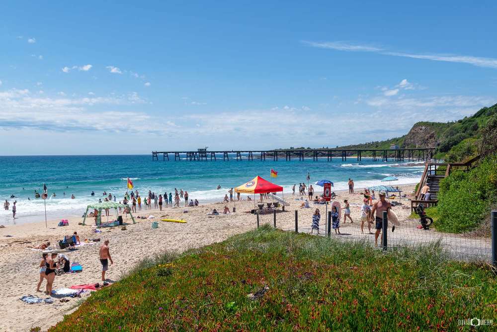 Visitors enjoying Catherine Hill Bay Beach with the historic coal-loading jetty in Lake Macquarie NSW