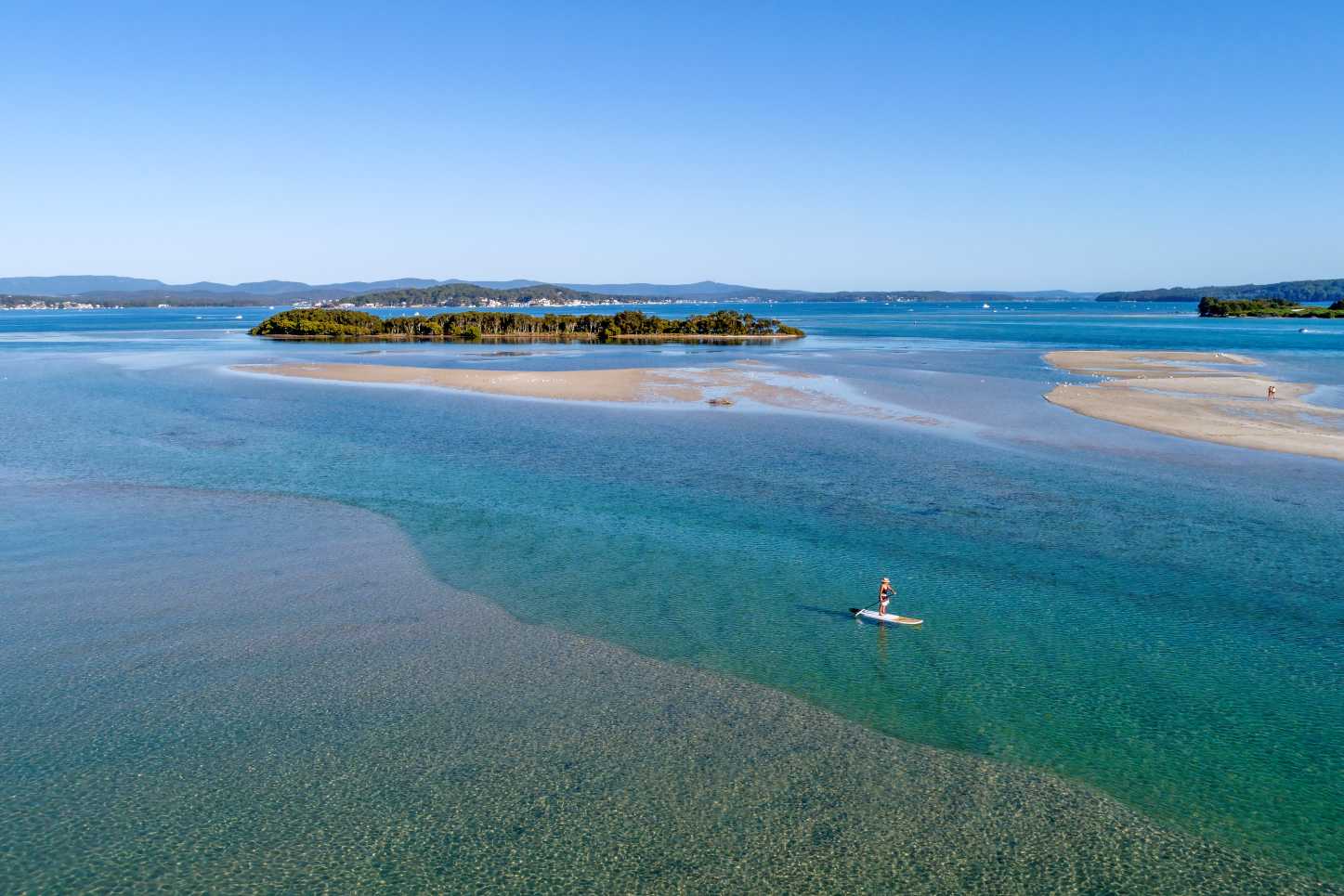Stand-up paddleboarder exploring turquoise water and sand islands on Lake Macquarie near Swansea NSW