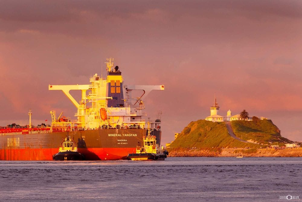 Coal ship departing Newcastle Harbour with Nobbys Lighthouse illuminated by golden evening light
