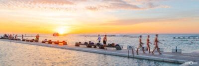 People enjoying a morning at Merewether Ocean Baths with swimmers, walkers and visitors embracing Newcastle's coastal lifestyle