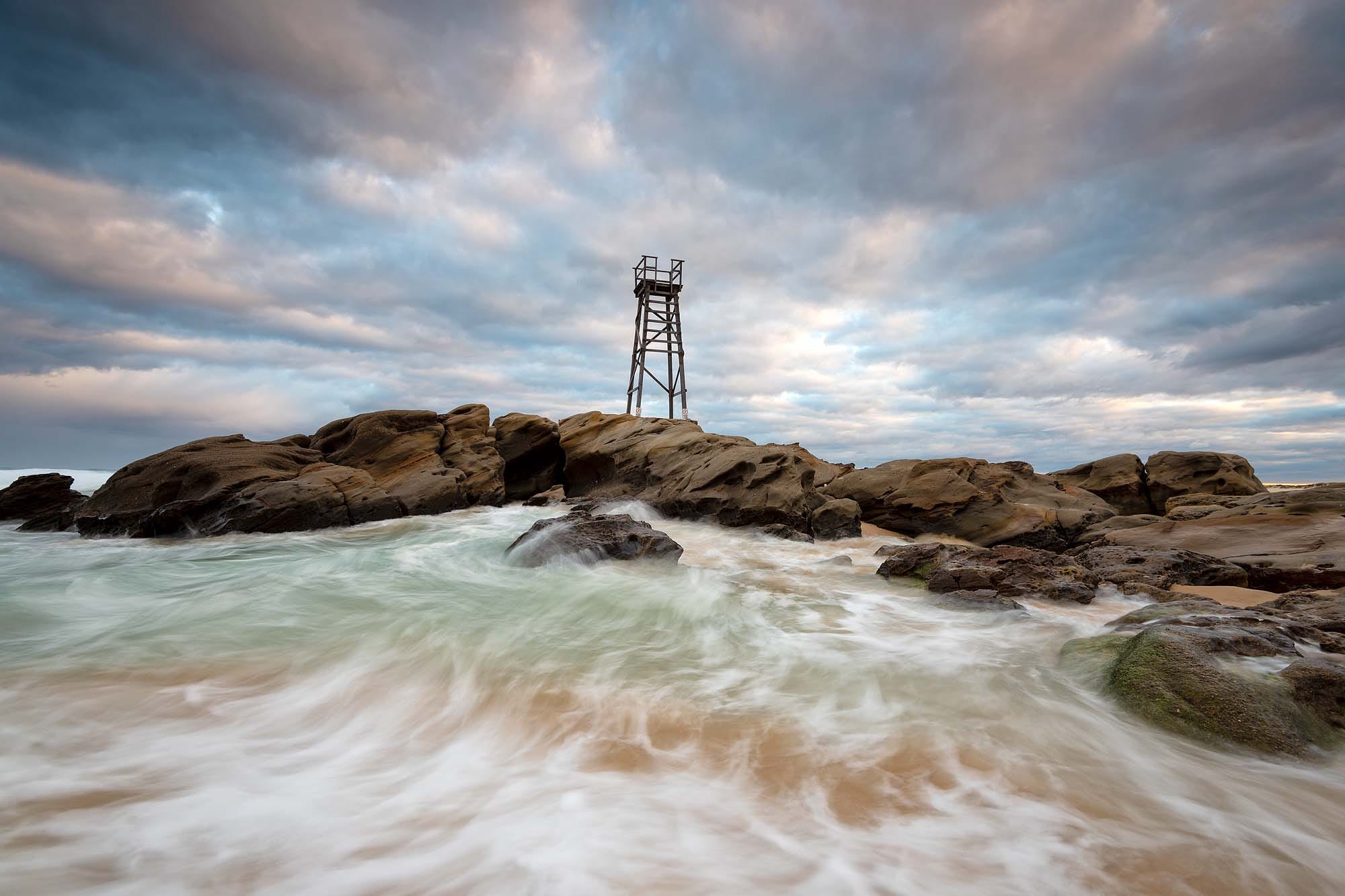 Ocean swell washing over the rocks below the Redhead Shark Tower during high tide at Redhead Beach NSW