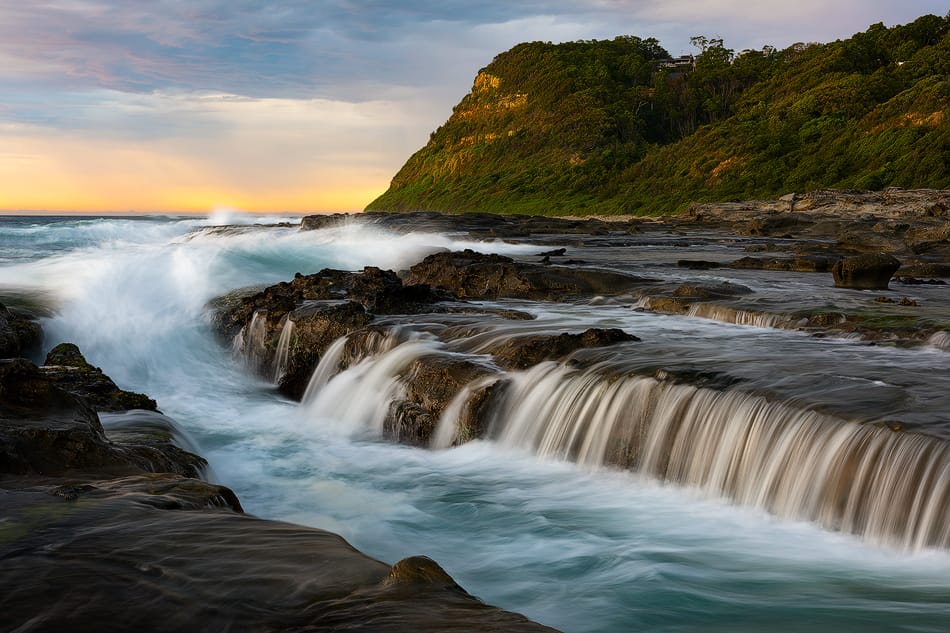 Sunrise over Dudley Beach rock platforms creating cascading waterfalls along the coastline