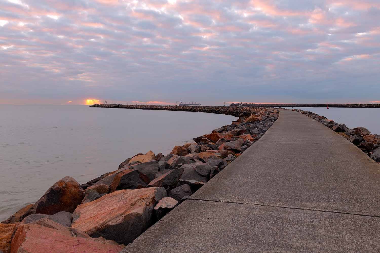 The Stockton Breakwall walking path stretches towards the harbour entrance at sunrise, offering views across Newcastle Harbour and the Pacific Ocean.