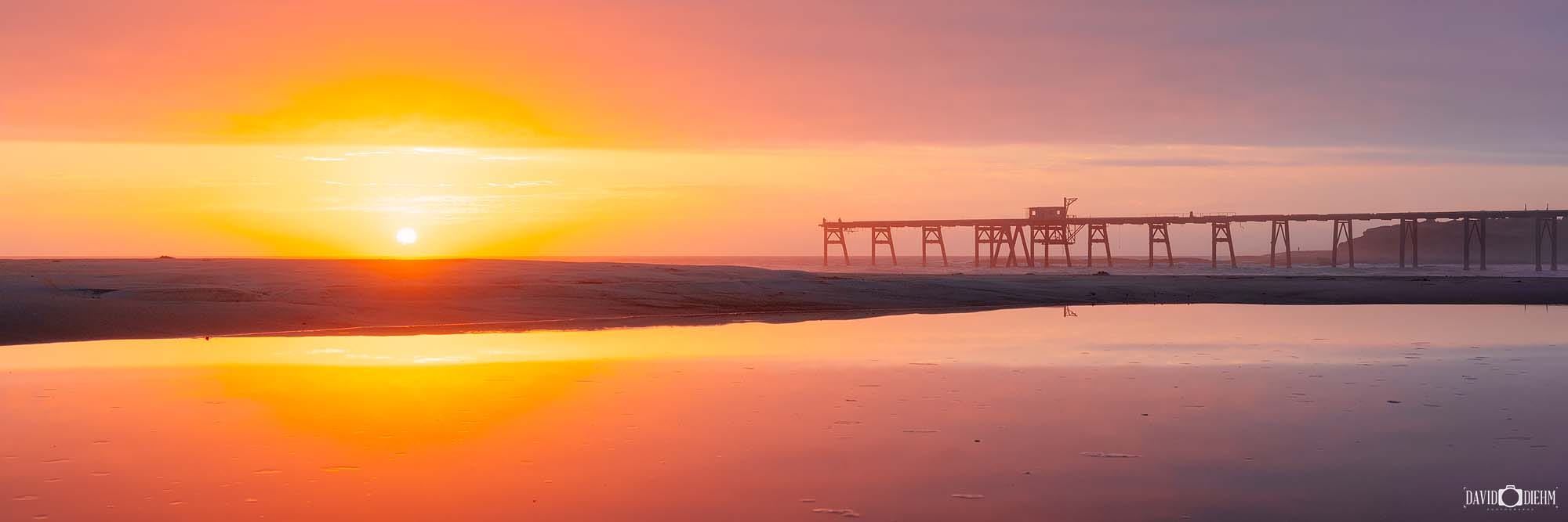 Panoramic sunrise at Catherine Hill Bay with calm water reflecting the sky and coastline.
