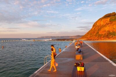 People enjoying a sunny morning at Merewether Ocean Baths with swimmers, walkers and visitors embracing Newcastle's coastal lifestyle.