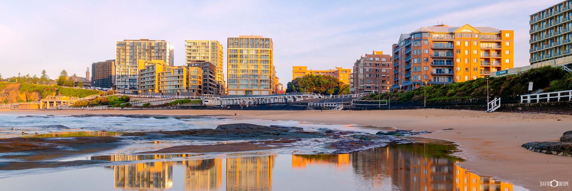 Wide panoramic view of sunrise at Newcastle Beach with vibrant reflections stretching across the beach