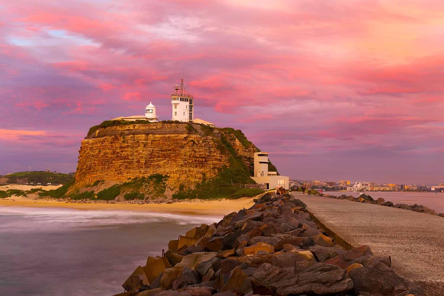 Nobbys Lighthouse viewed from Nobbys Breakwall at sunrise, with colourful clouds reflecting above Newcastle Harbour and the Pacific Ocean.