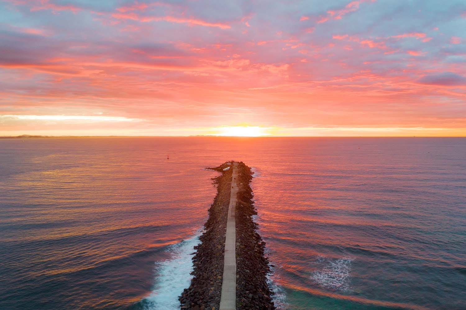 Sunrise over the Nobbys Breakwall extending into the Pacific Ocean at Nobbys Headland in Newcastle NSW.
