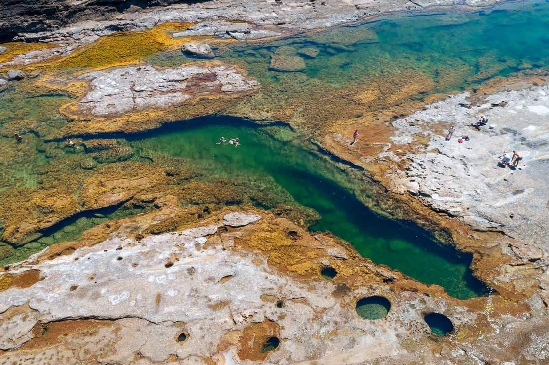 Natural ocean rock pool near Catherine Hill Bay with visitors enjoying the sheltered water beside the Pacific Ocean and rugged coastline.