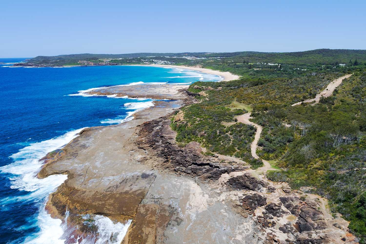 Aerial view of the Catherine Hill Bay Coastal Walk leading towards the rock pools, with rugged coastal cliffs, ocean platforms and pristine beaches stretching along the coastline.