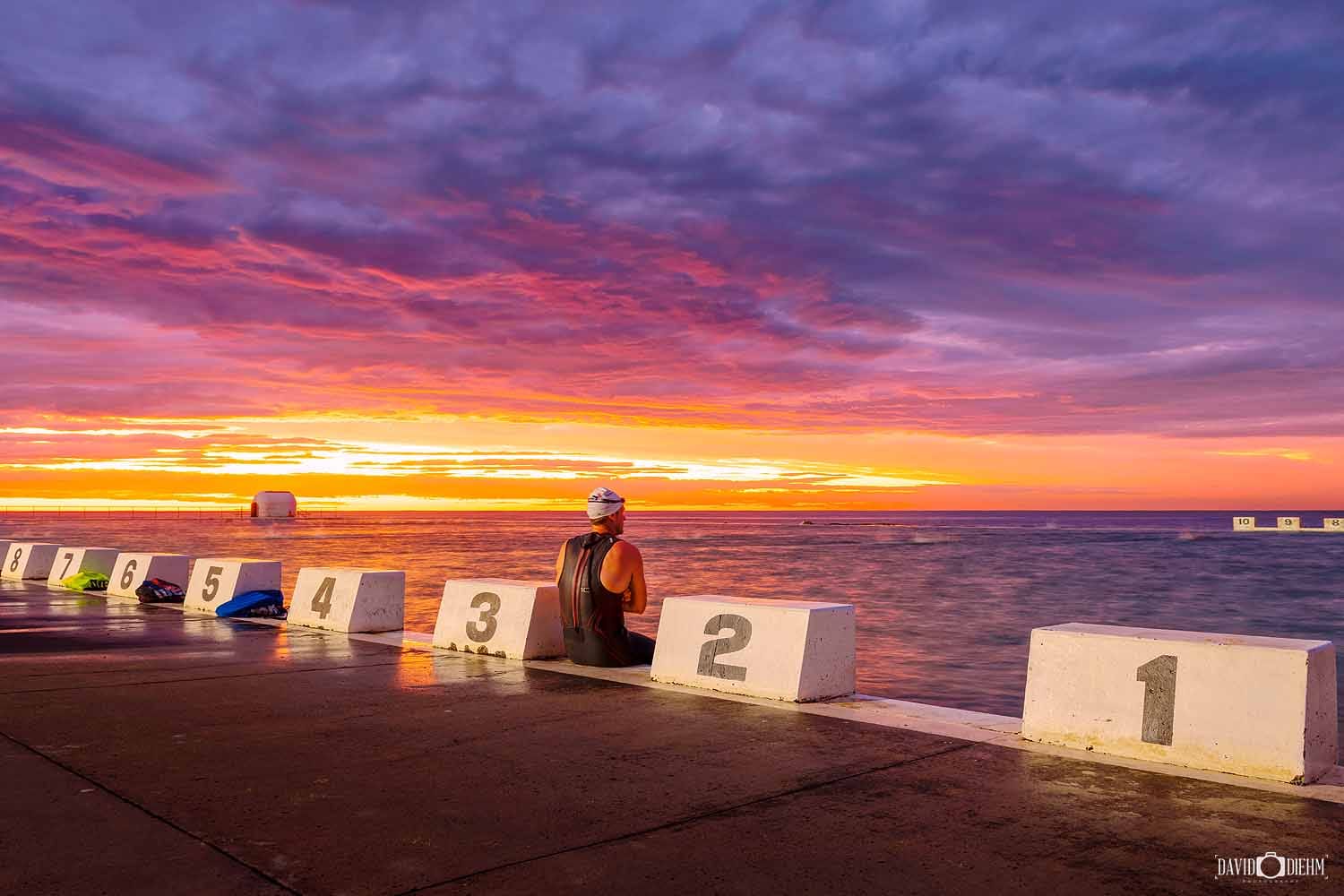 A swimmer watches sunrise from Merewether Ocean Baths in Newcastle NSW