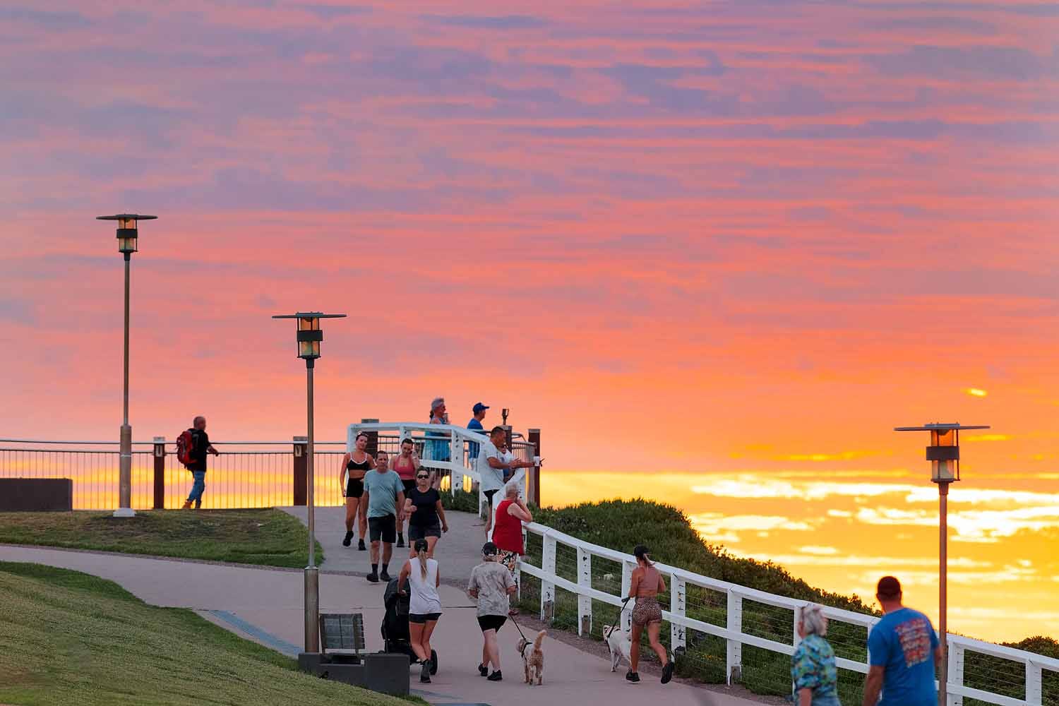 Walkers, joggers and dog owners enjoying sunrise along the Bathers Way Coastal Walk in Newcastle as colourful morning skies light up the coastline.