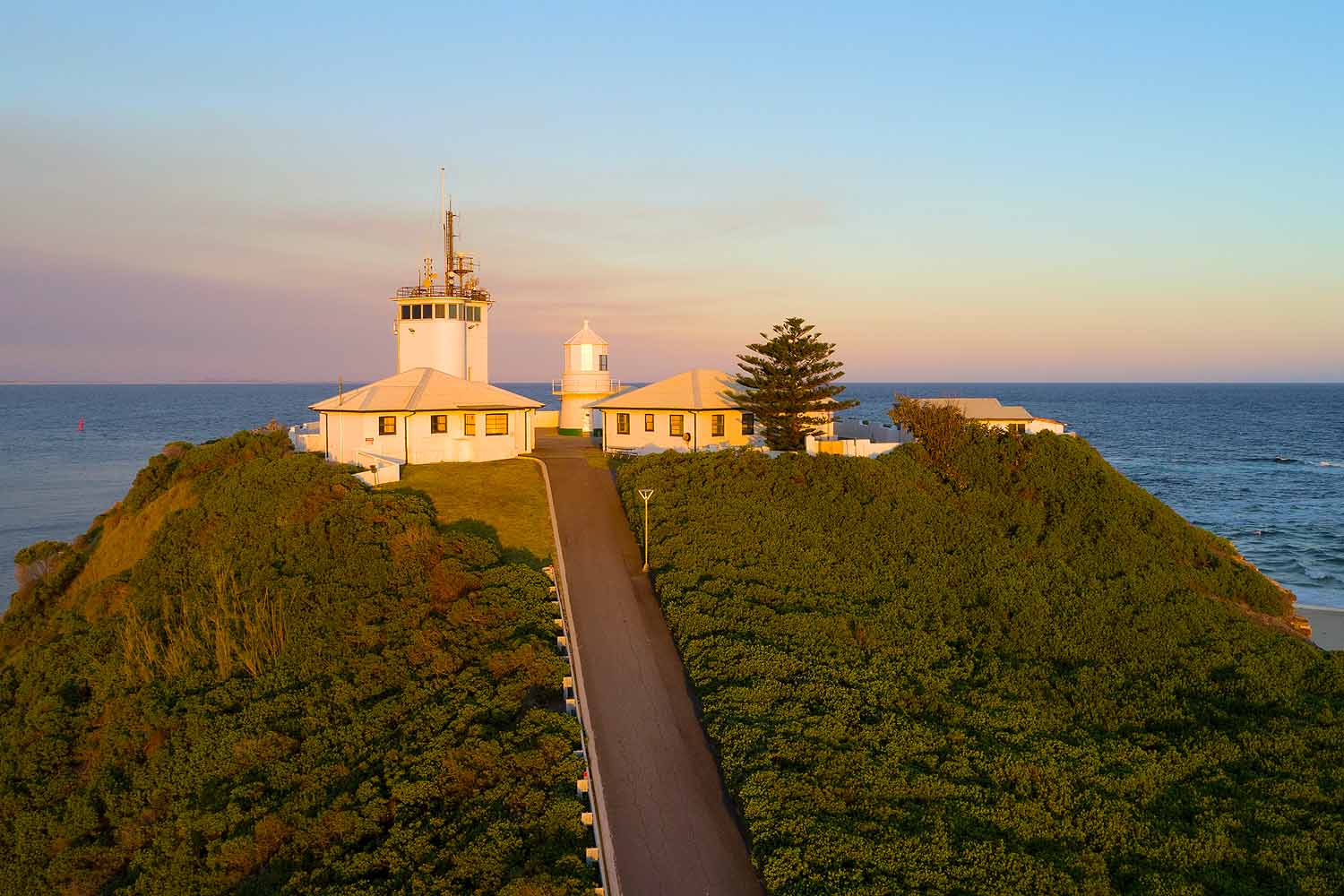 Nobbys Lighthouse viewed from Nobbys Headland Walk in Newcastle, NSW, illuminated by golden afternoon light overlooking the Pacific Ocean.