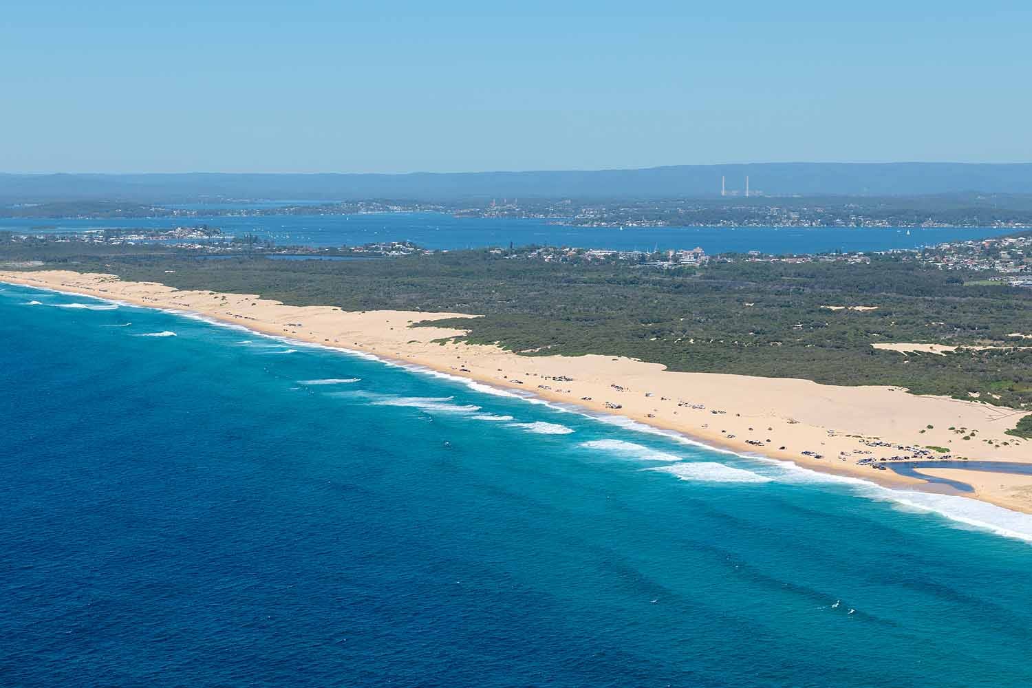 Aerial panorama of Nine Mile Beach in Lake Macquarie, showing kilometres of golden sand, turquoise ocean, coastal dunes and the coastline stretching between Blacksmiths and Redhead.