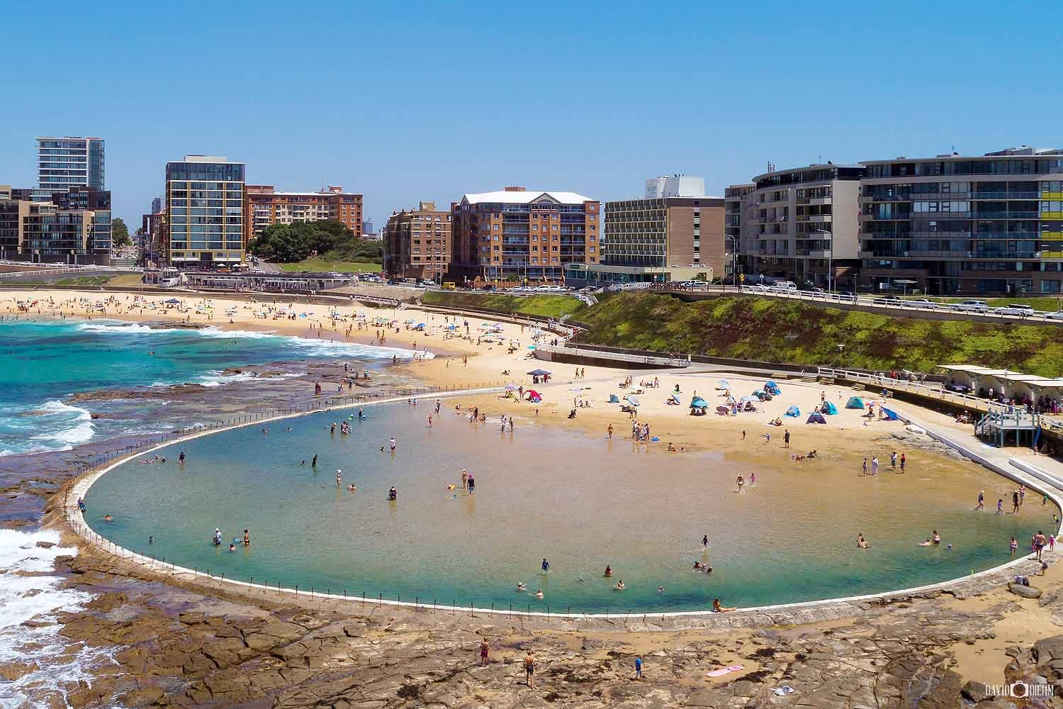 Aerial view of Newcastle Ocean Baths and Newcastle Beach on a busy summer day in Newcastle NSW.