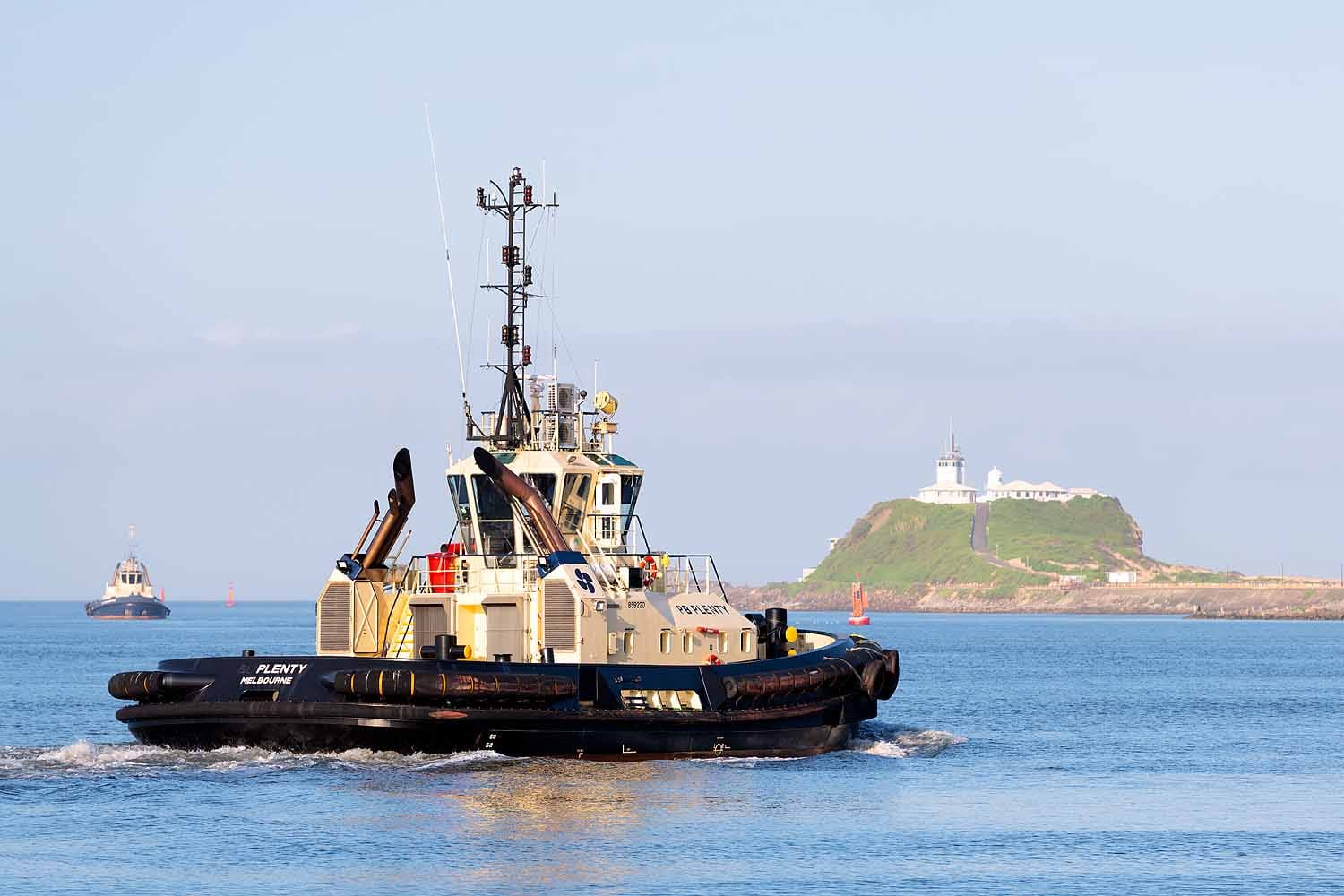 Harbour tugboat travelling across Newcastle Harbour with Nobbys Lighthouse and headland visible in the background.