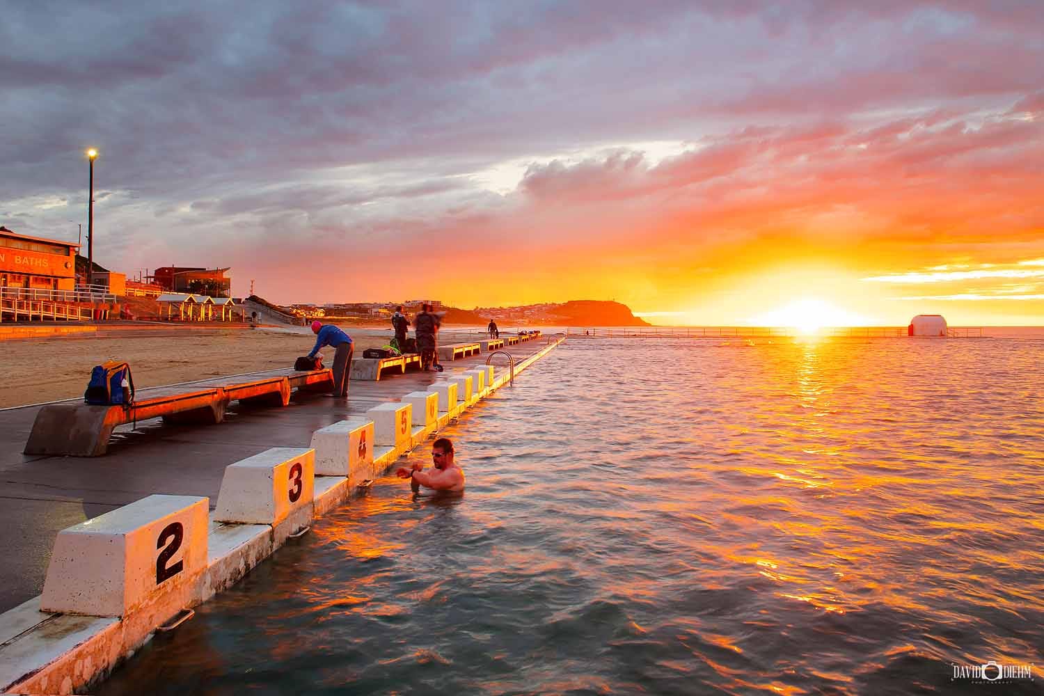 Swimmers enjoying sunrise at Merewether Ocean Baths with golden morning light reflecting across the ocean pool.