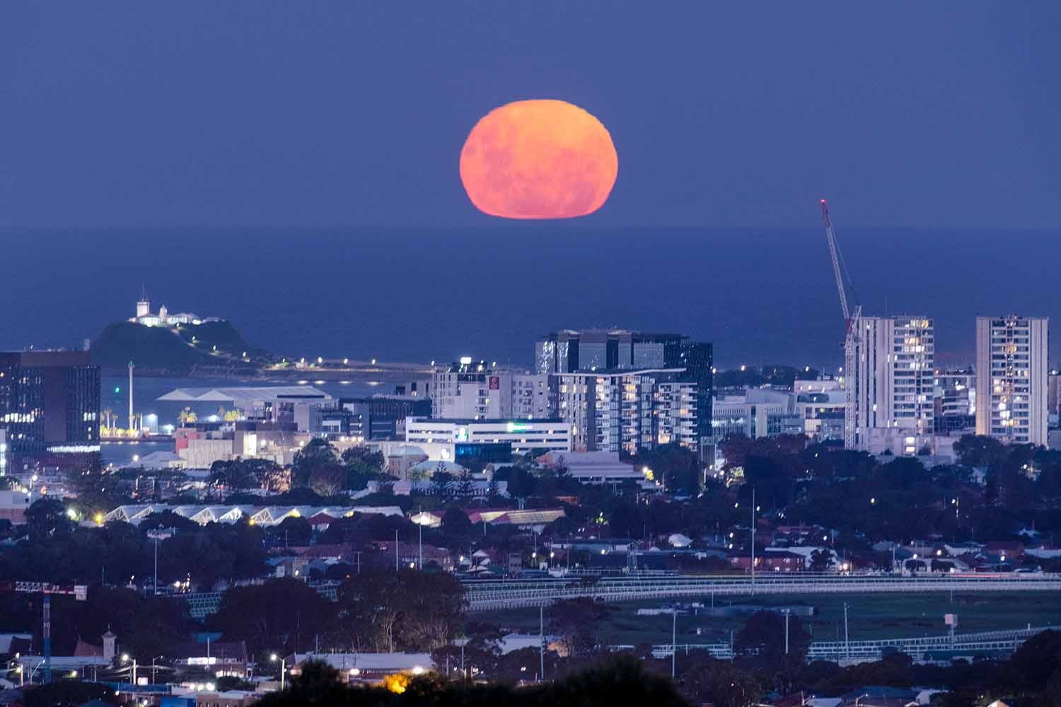 A full moon rising above Newcastle Harbour and Nobbys Lighthouse viewed from New Lambton Heights Lookout.