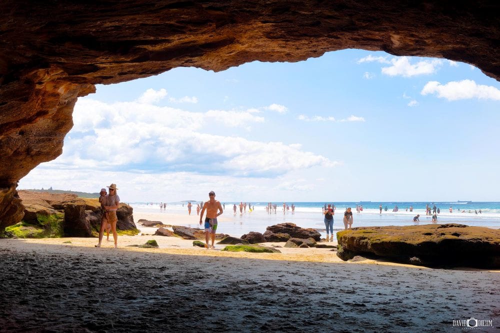 View from inside a sea cave at Caves Beach looking across the beach and ocean at low tide.