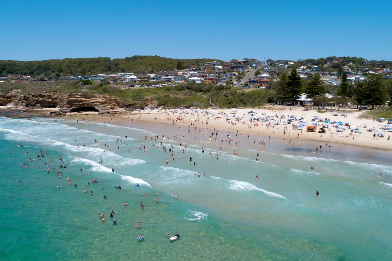 Aerial view of families swimming and enjoying Caves Beach on a sunny summer day in Lake Macquarie NSW.