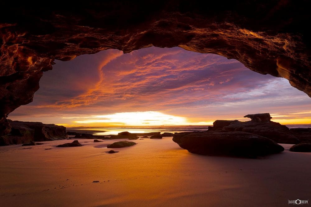 Sunrise viewed from inside the sea caves at Caves Beach with colourful clouds and sandstone formations.