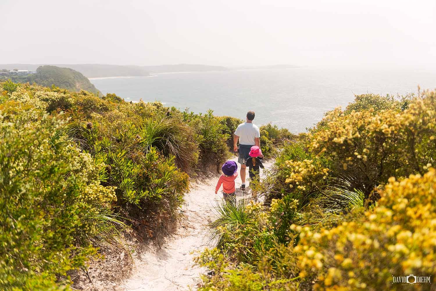 Family walking along the Awabakal Coastal Walk through native coastal heath overlooking the coastline in Lake Macquarie NSW.