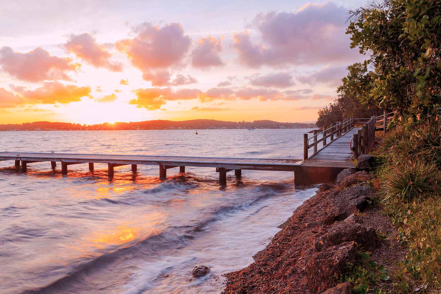 Sunset over Green Point Reserve in Lake Macquarie, featuring the timber jetty, lakeside walking path, gentle waves and colourful reflections across the water.
